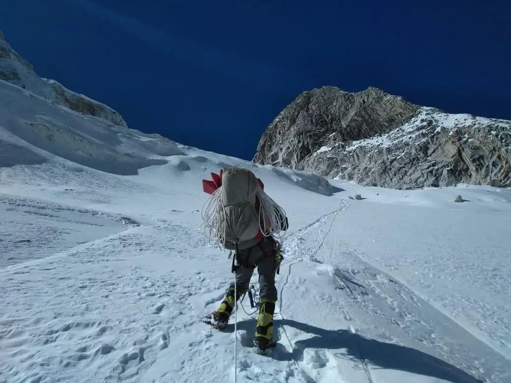 Mountaineer ascending snow-covered slope towards Larkya Peak of Manaslu, Nepal, carrying climbing rope and gear under clear blue sky